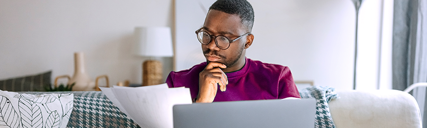 Person reading print and online document using laptop