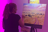 An artist at an Art Battle. She is panting a landscape with vivid colours.