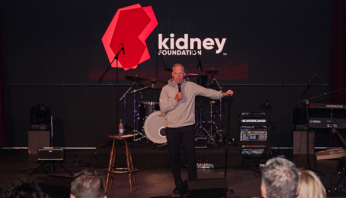 Gerry Dee on stage, leaning on a microphone stand